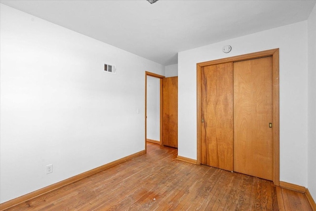 unfurnished bedroom with visible vents, baseboards, a closet, and hardwood / wood-style floors