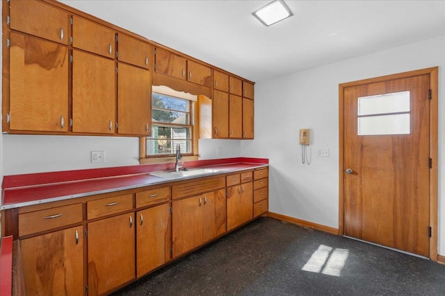 kitchen featuring brown cabinets, dark floors, baseboards, and a sink