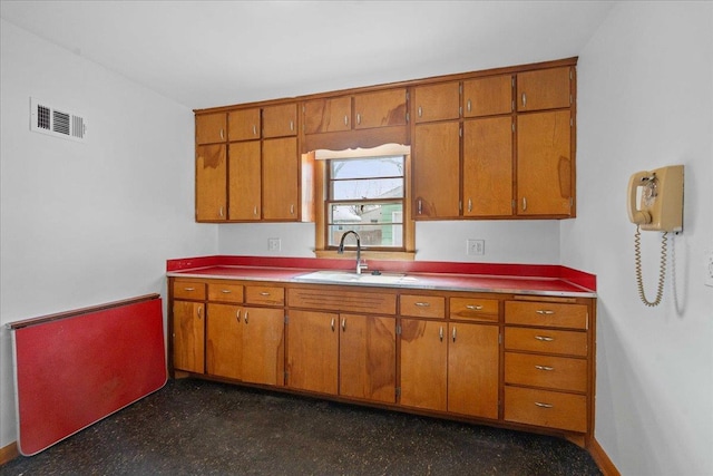 kitchen featuring visible vents, brown cabinets, baseboards, and a sink