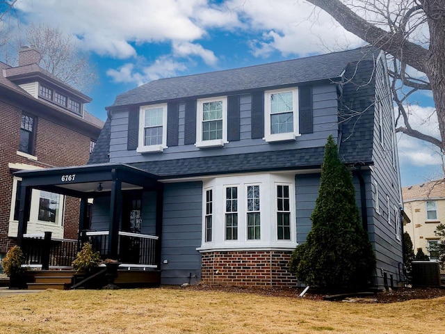 view of front of property featuring a gambrel roof, roof with shingles, a front lawn, a porch, and brick siding