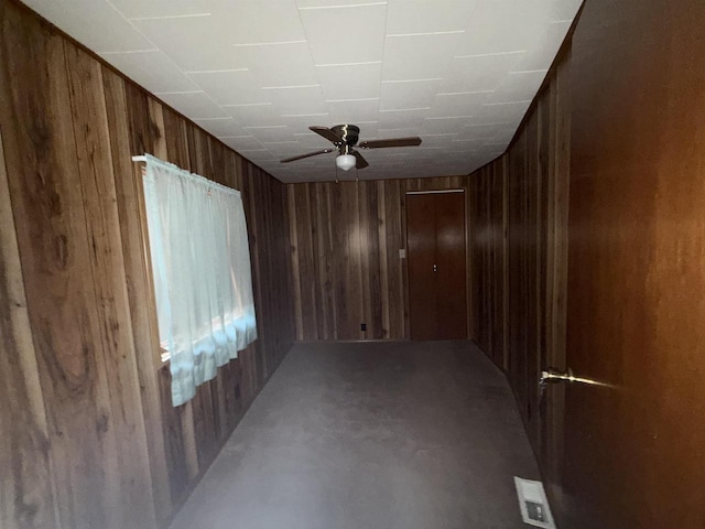 spare room featuring wood walls, ceiling fan, visible vents, and concrete flooring