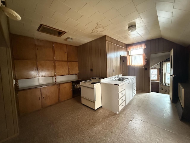 kitchen featuring lofted ceiling, wood walls, a sink, white range with electric stovetop, and brown cabinets