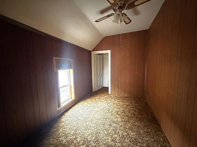 carpeted spare room with lofted ceiling, a ceiling fan, and wooden walls