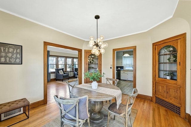 dining space featuring light wood finished floors, a notable chandelier, crown molding, and baseboards