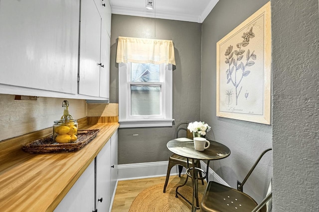 kitchen featuring wood counters, white cabinetry, light wood-style floors, crown molding, and baseboards