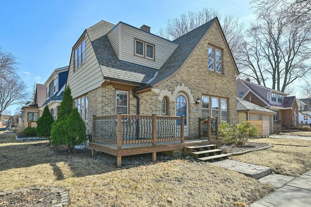 view of front of home with roof with shingles, an attached garage, a chimney, a deck, and brick siding