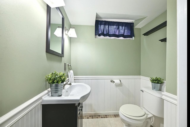 half bathroom with a wainscoted wall, toilet, vanity, and tile patterned flooring