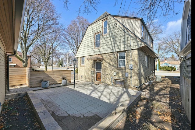 rear view of property featuring brick siding, a patio area, fence, and a gambrel roof