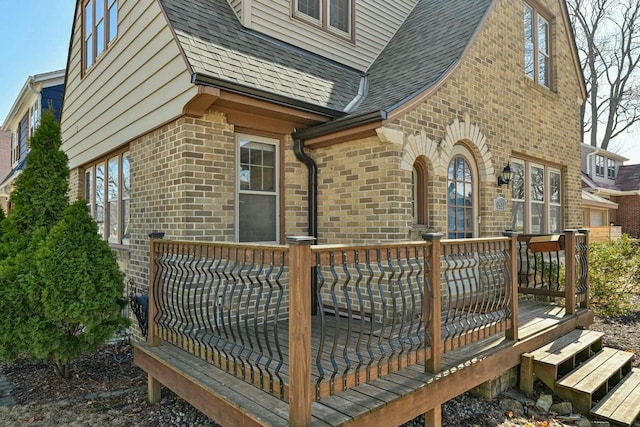 view of property exterior with brick siding, roof with shingles, and a wooden deck