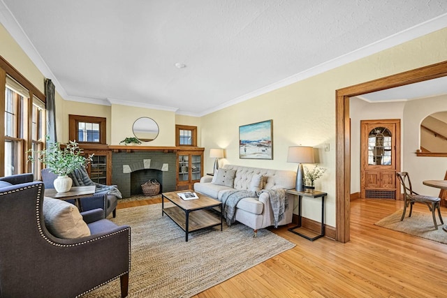 living area with a fireplace, baseboards, crown molding, and light wood-style floors