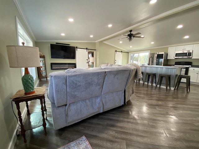 living area with a barn door, crown molding, dark wood-style flooring, and vaulted ceiling