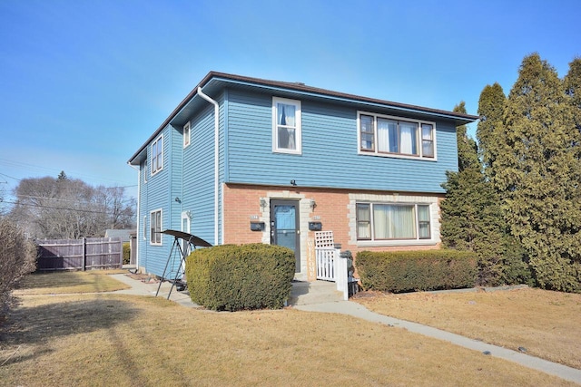 view of front facade featuring brick siding, a front yard, and fence