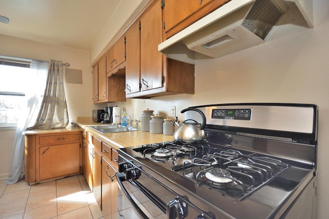 kitchen with light countertops, light tile patterned flooring, a sink, under cabinet range hood, and stainless steel gas range oven