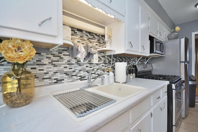 kitchen featuring decorative backsplash, appliances with stainless steel finishes, white cabinetry, a sink, and light tile patterned flooring