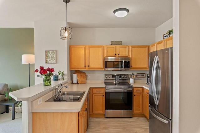 kitchen featuring a peninsula, a sink, hanging light fixtures, appliances with stainless steel finishes, and light countertops