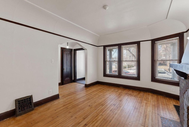 spare room featuring light wood-style floors, arched walkways, and baseboards