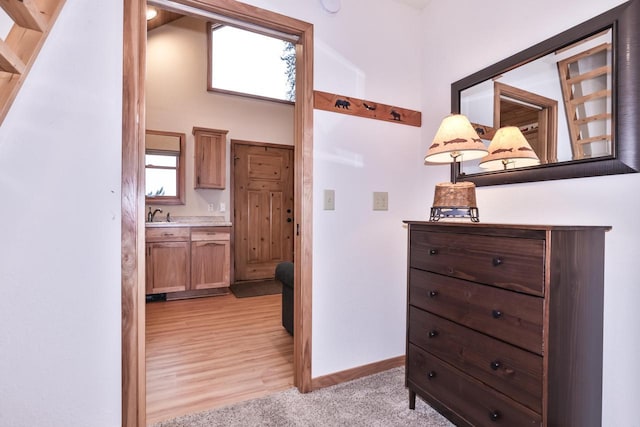 hallway with light carpet, a sink, and baseboards