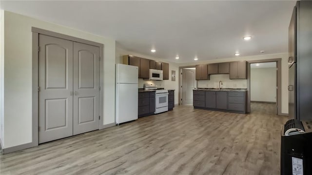 kitchen featuring light wood finished floors, recessed lighting, a sink, white appliances, and baseboards