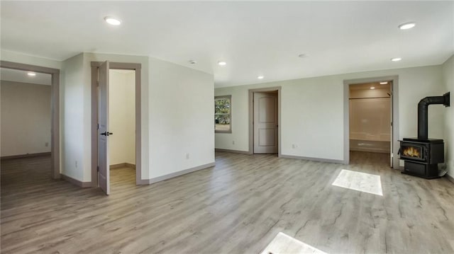 unfurnished living room featuring light wood-style floors, a wood stove, and baseboards