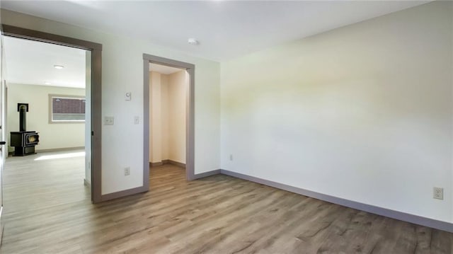 empty room with light wood-style floors, a wood stove, and baseboards