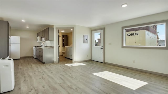 unfurnished living room with recessed lighting, baseboards, electric panel, light wood finished floors, and washer / dryer