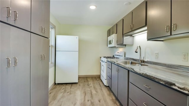 kitchen with white appliances, a sink, baseboards, light wood-type flooring, and light stone countertops