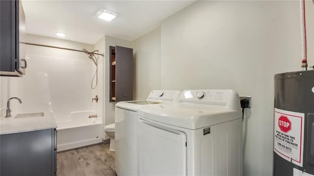 laundry area with laundry area, separate washer and dryer, a sink, light wood-style floors, and water heater