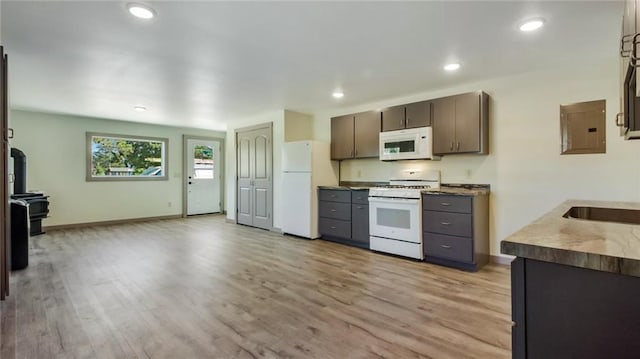 kitchen with white appliances, electric panel, baseboards, a wood stove, and light wood-type flooring