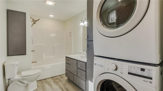 bathroom with toilet, wood finished floors, vanity, stacked washer and clothes dryer, and washtub / shower combination