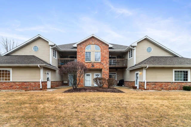 view of front of property featuring roof with shingles, brick siding, a front lawn, and a balcony