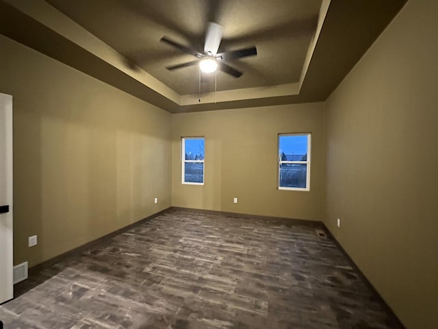 spare room with baseboards, visible vents, a raised ceiling, ceiling fan, and wood finished floors