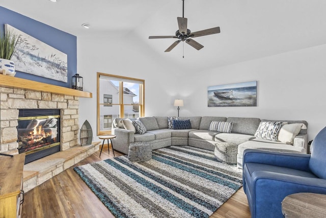 living area featuring ceiling fan, vaulted ceiling, wood finished floors, and a stone fireplace