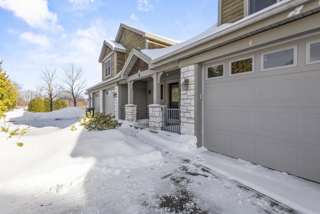 snow covered property with an attached garage and stone siding