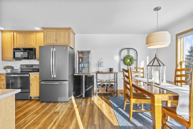 kitchen with light wood-style flooring, stainless steel appliances, light countertops, light brown cabinetry, and pendant lighting