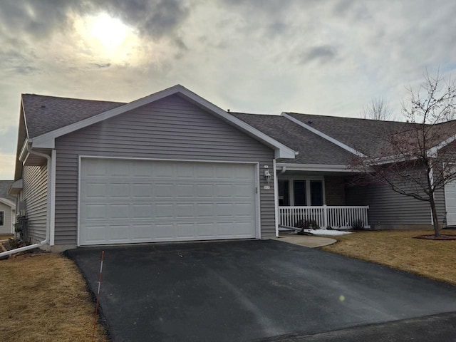 ranch-style home featuring a porch, an attached garage, a shingled roof, and aphalt driveway