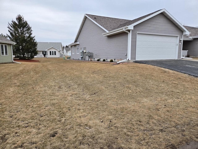 view of home's exterior featuring a garage, a shingled roof, aphalt driveway, and a yard