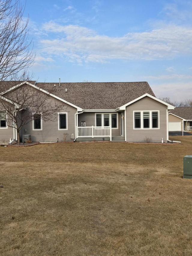 rear view of house featuring a shingled roof and a yard