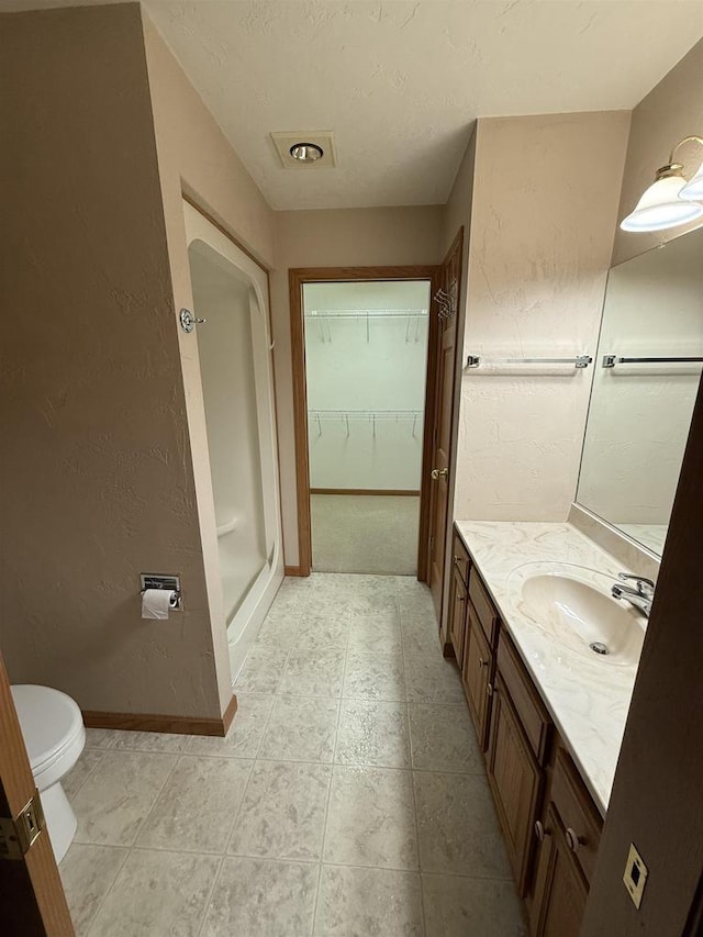 bathroom with a spacious closet, toilet, a stall shower, vanity, and baseboards