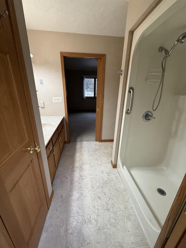 bathroom with a textured ceiling, a shower stall, vanity, baseboards, and tile patterned floors