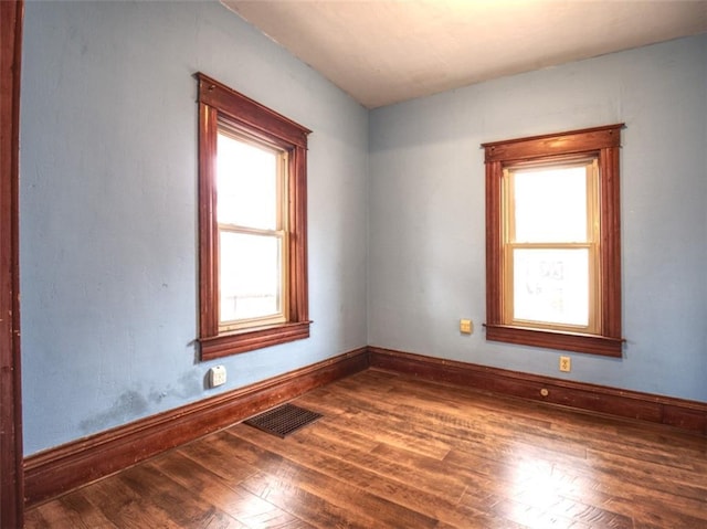 empty room with baseboards, visible vents, and hardwood / wood-style floors