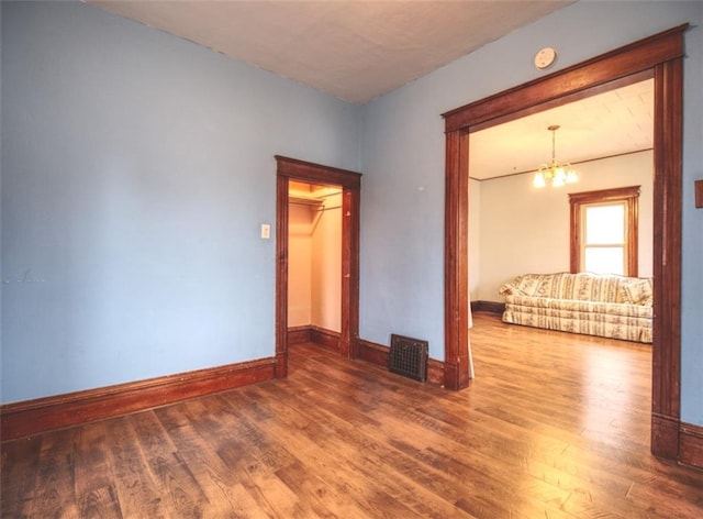 spare room with a notable chandelier, baseboards, and wood finished floors