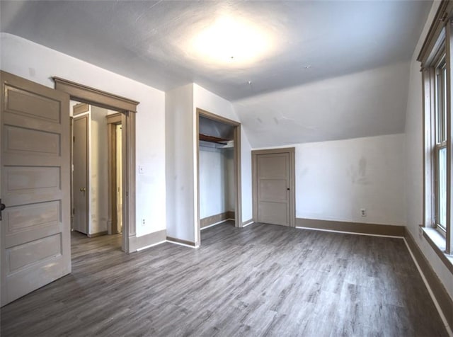 unfurnished bedroom featuring vaulted ceiling, a closet, dark wood-style floors, and baseboards