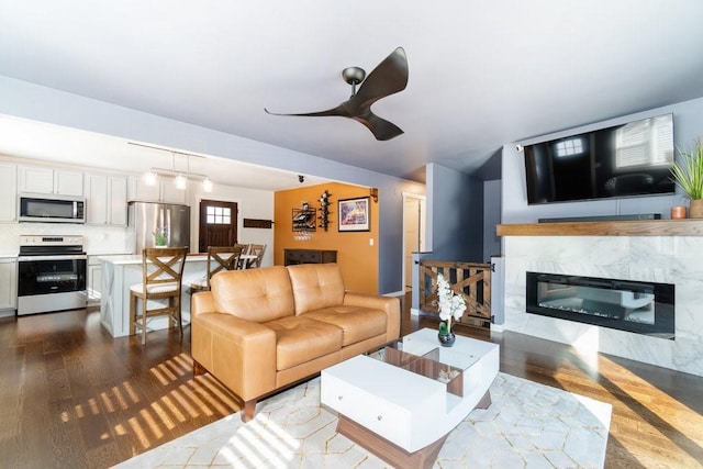 living room with a ceiling fan, dark wood-style flooring, and a premium fireplace