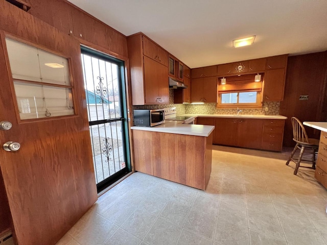 kitchen featuring under cabinet range hood, a peninsula, white electric range, brown cabinets, and stainless steel microwave