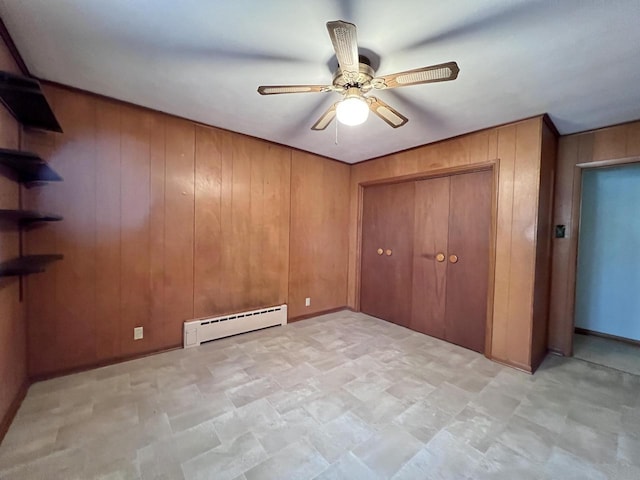 unfurnished bedroom featuring wood walls, a baseboard radiator, a ceiling fan, and a closet