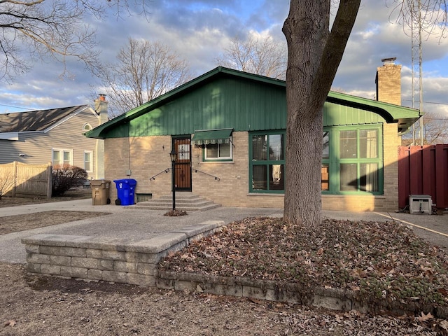 rear view of property with entry steps, a chimney, fence, and brick siding