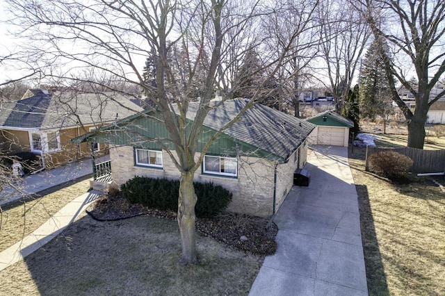 view of home's exterior with an outbuilding, brick siding, a detached garage, roof with shingles, and fence