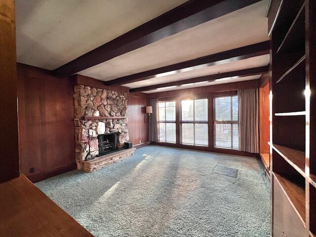 carpeted living area featuring wooden walls, beam ceiling, and a stone fireplace