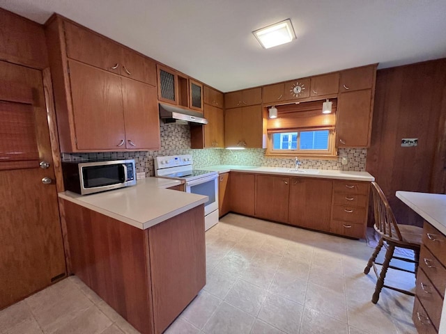 kitchen featuring white electric stove, stainless steel microwave, brown cabinetry, a peninsula, and under cabinet range hood