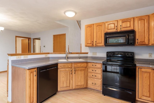 kitchen featuring light wood-style flooring, brown cabinets, a peninsula, black appliances, and a sink